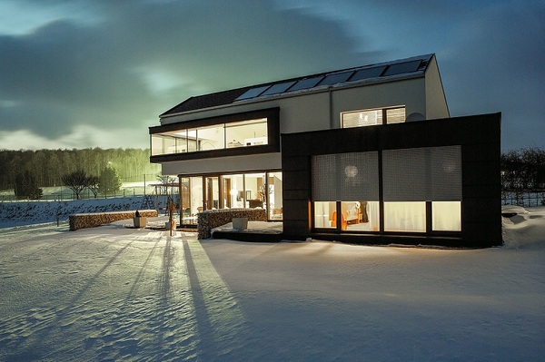 Modernes Einfamilienhaus mit großen Fenstern im Winter bei beleuchtetem Innenraum.