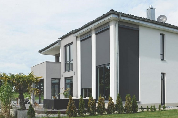 Modernes Einfamilienhaus mit großen Fenstern und außenliegenden Sonnenschutz-Rollläden.