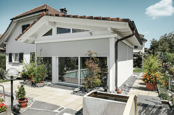 Modernes Gartenhaus mit Sonnenschutz-Rollladen und Terrasse in gepflegtem Garten.