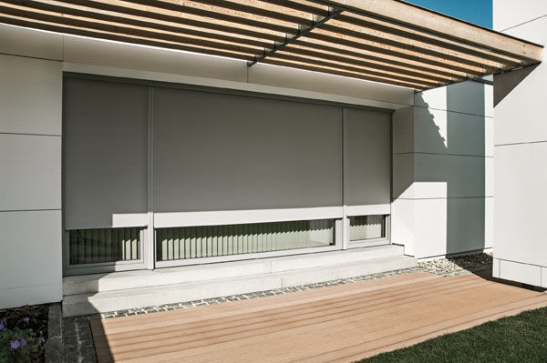 Moderne Terrassenüberdachung mit Sonnenschutz und großen Fensterflächen am Haus.